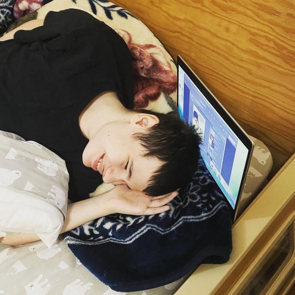 A young man lying in a Sleep Safe bed resting his head on a laptop.