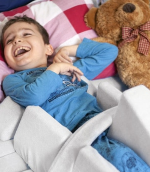 A young child lying in a SleepSafe bed with a teddy bear lying next to them.