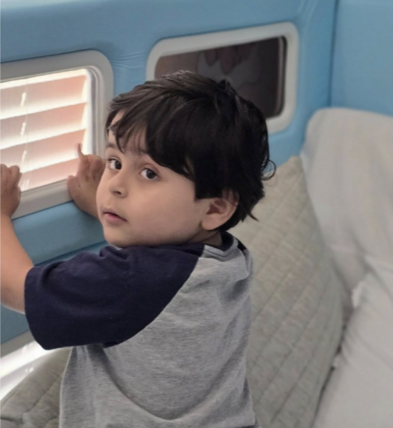 A boy sitting in a SleepSafe bed with his hands on one of the mesh windows