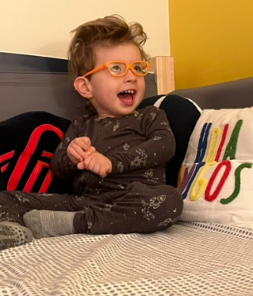 A young boy wearing glasses and seated in a SleepSafe bed.