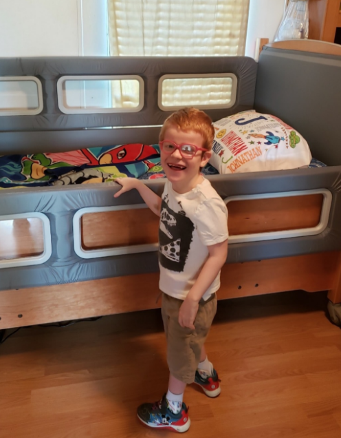 A young boy wearing glasses standing next to a SleepSafe bed