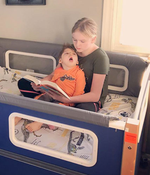 A woman seated in a SleepSafe bed reading a book to a child seated on her lap.