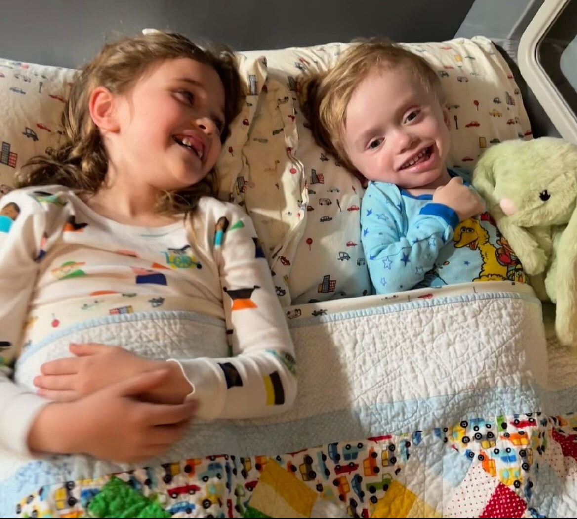 Two young children wearing pajamas and lying in bed