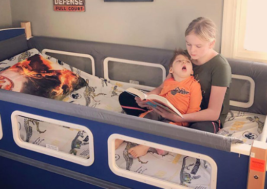 A woman seated in a SleepSafe bed reading a book to a child seated on her lap.