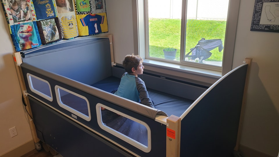 A boy sitting in a SleepSafe bed looking out a window.