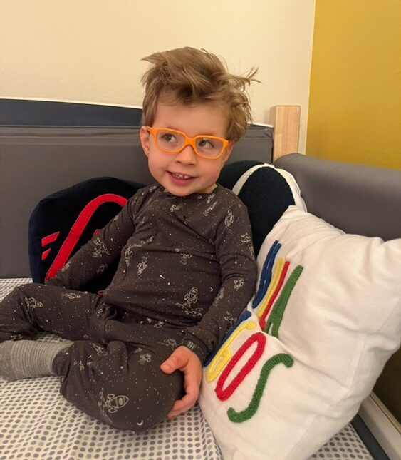 A young boy wearing glasses and sitting in a Sleep Safe bed.