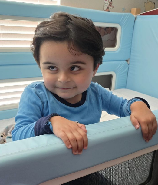 A toddler standing up in a SleepSafe bed and holding onto the railing.