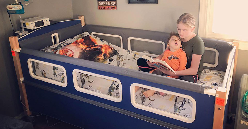 A woman seated in a SleepSafe bed reading a book to a child seated on her lap.